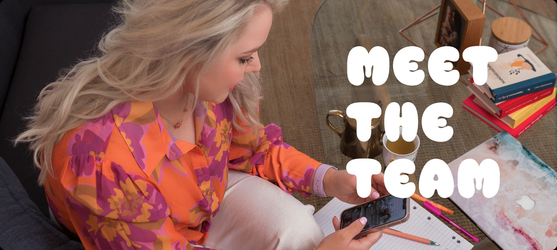 Flic from Your Fan Club sitting at a desk and looking at her phone, with ‘Meet the Team’ text displayed beside her.